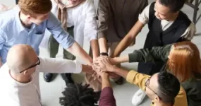 A group of adults in a circle with their hands stacked in the centre.